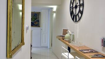 A dining area with a wooden table, white chairs, a large wall clock, and a mirror.