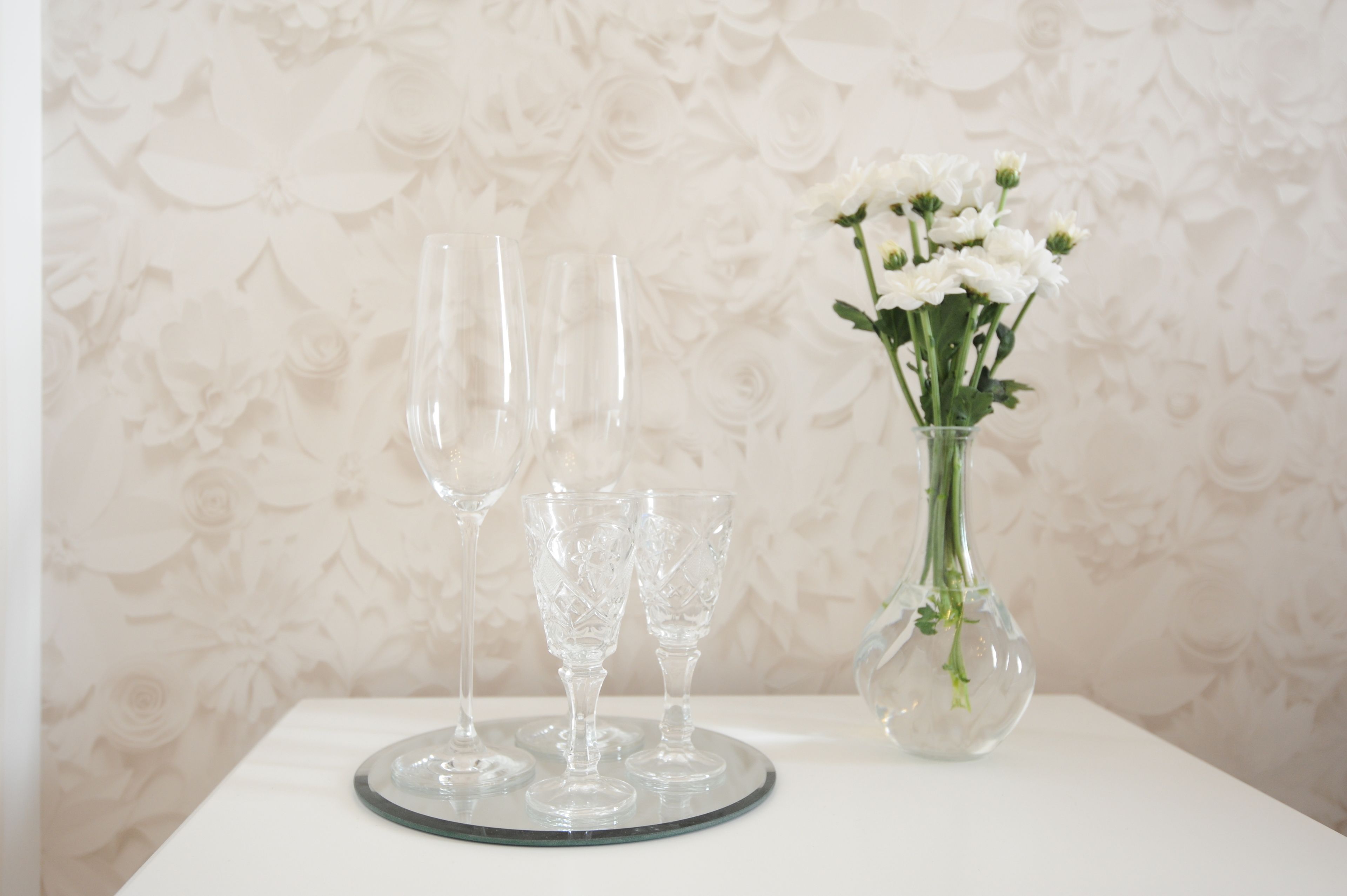 A table with three clear glass wine glasses and a vase with white flowers.
