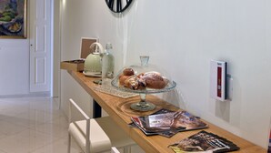 A kitchen counter with a glass display case containing pastries, a kettle, and a bottle of hand soap. There are magazines on the counter and a clock on the wall. - Residenza Borbonica (Naples)