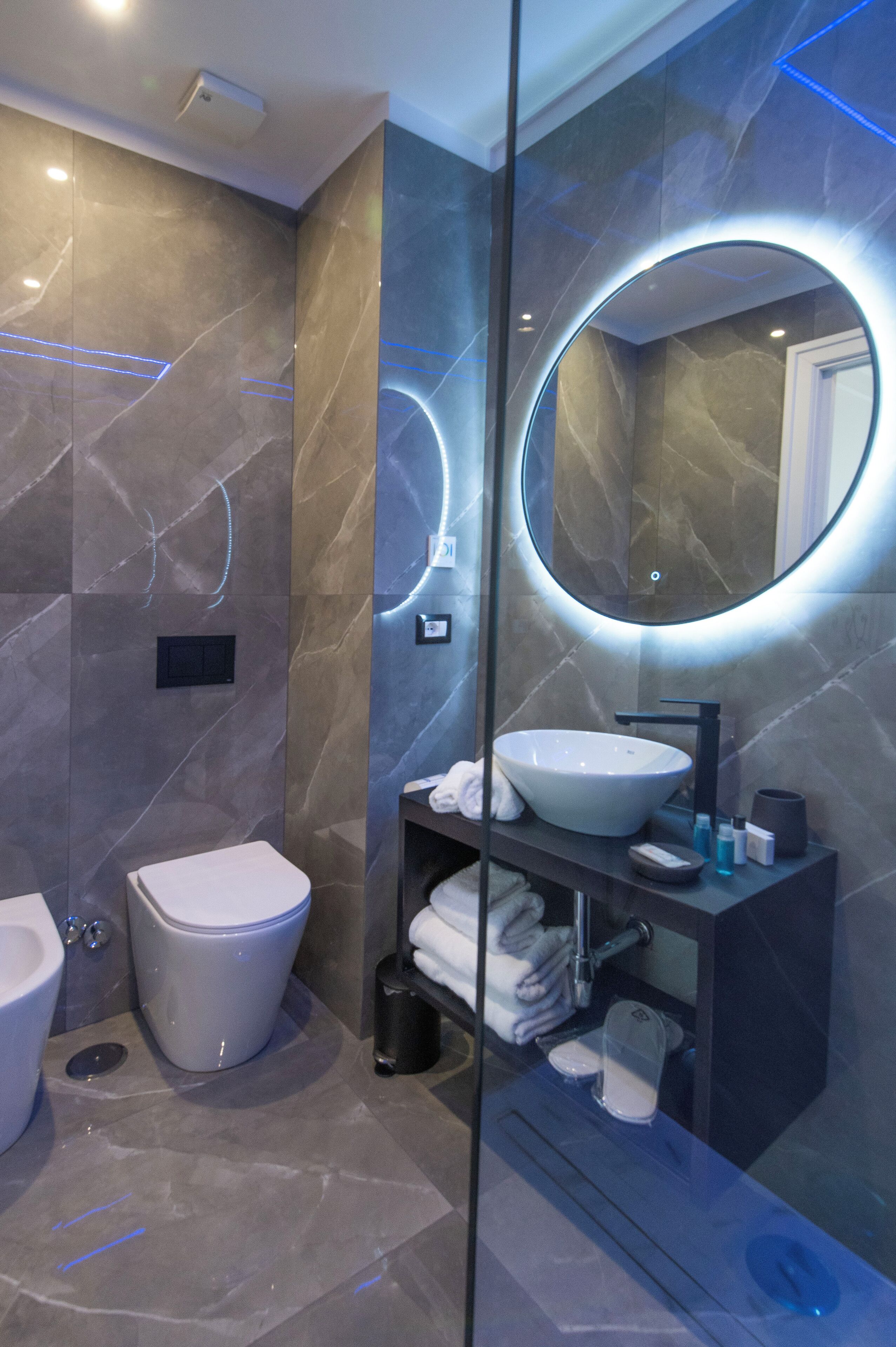 A modern bathroom with a large oval mirror, a white sink, and a toilet.