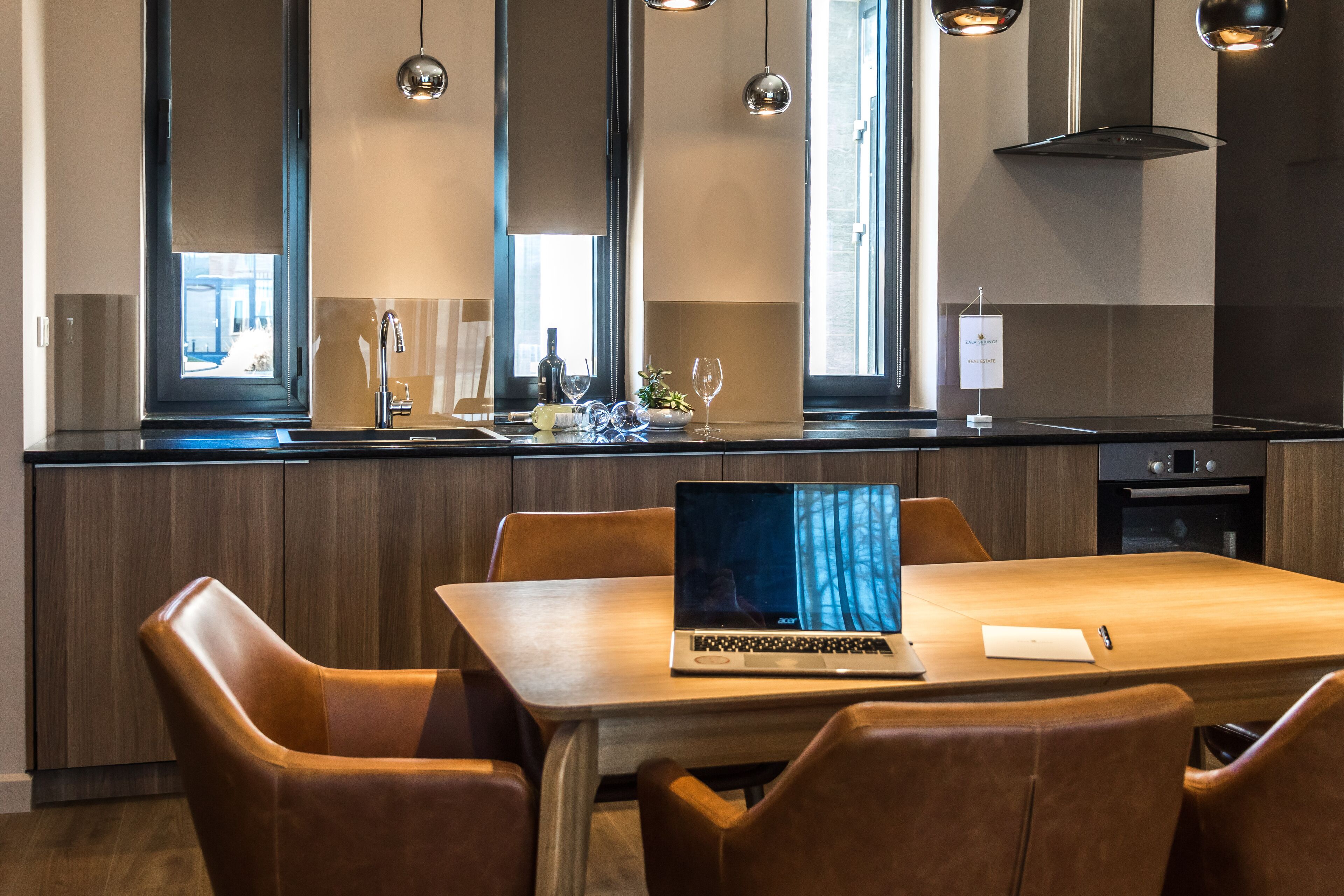 Una cocina moderna con comedor, que incluye un ordenador portátil sobre la mesa, armarios de madera e iluminación colgante.