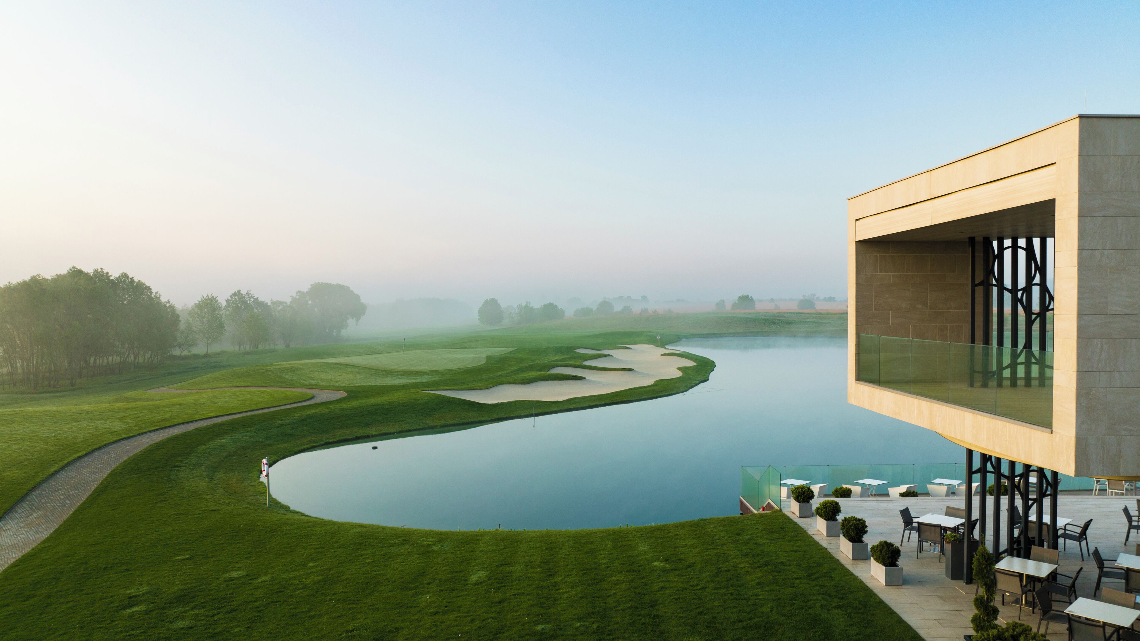 A modern building with a glass facade overlooking a golf course and a river.