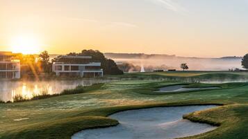 A golf course with bunkers and a body of water reflecting the sun.