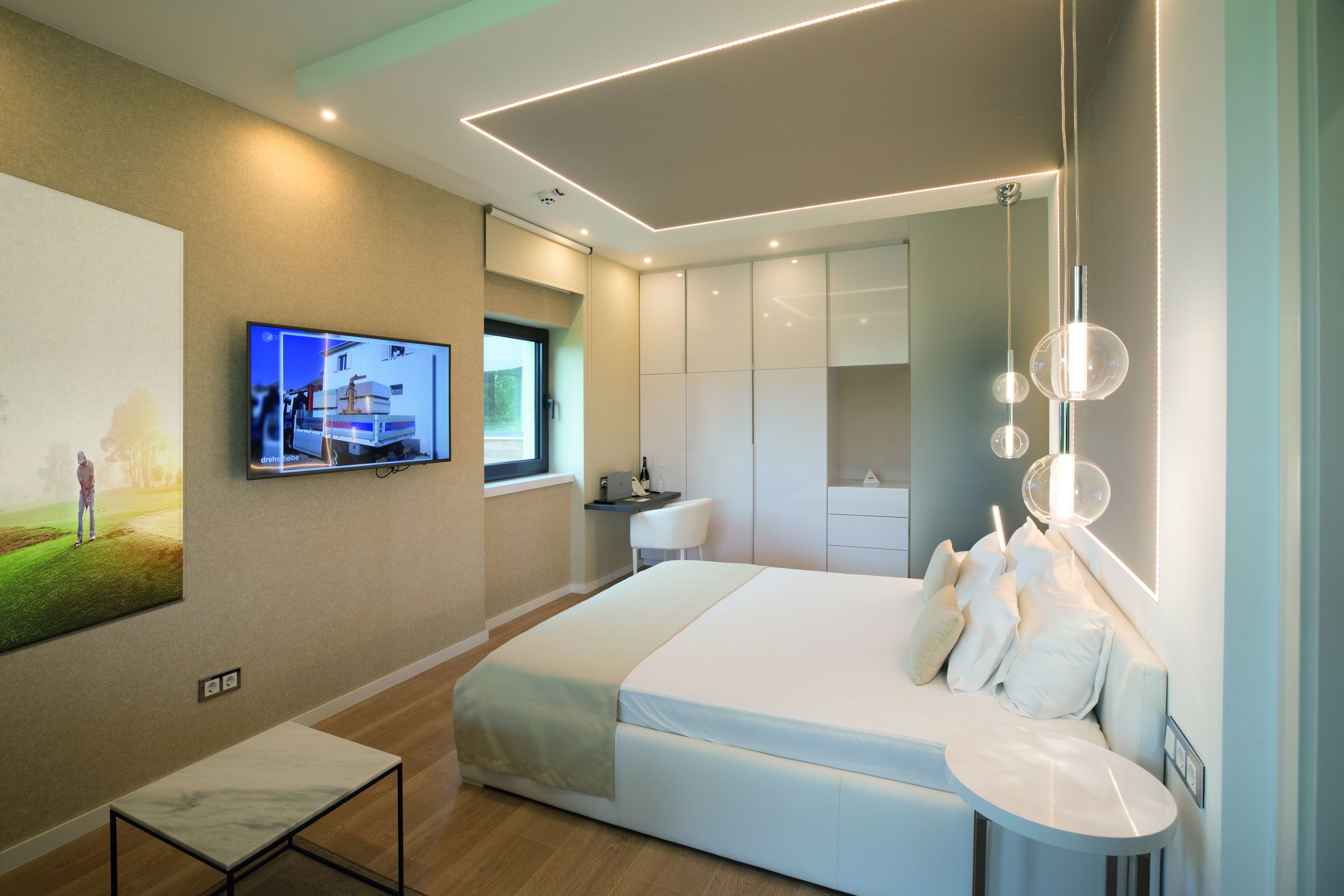 Een moderne slaapkamer met een groot bed, een aan de muur bevestigde televisie en een bureau met een stoel.