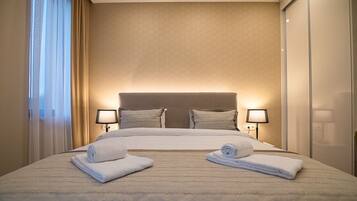 Quarto de hotel com uma cama grande, duas luminárias de cabeceira e vista para a cidade pela janela.