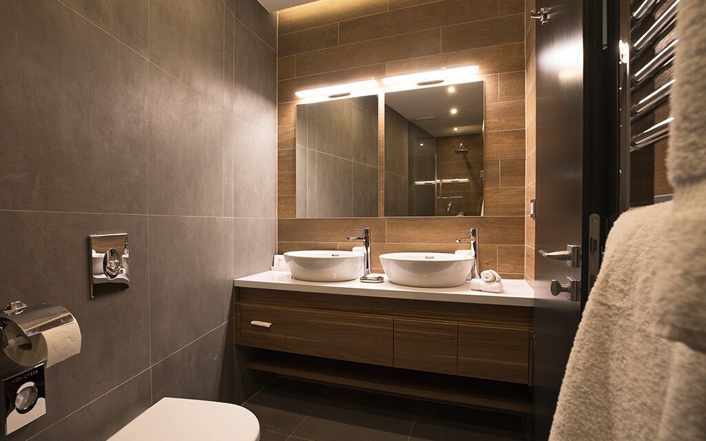 A modern bathroom with two sinks, a large mirror, and a towel rack.