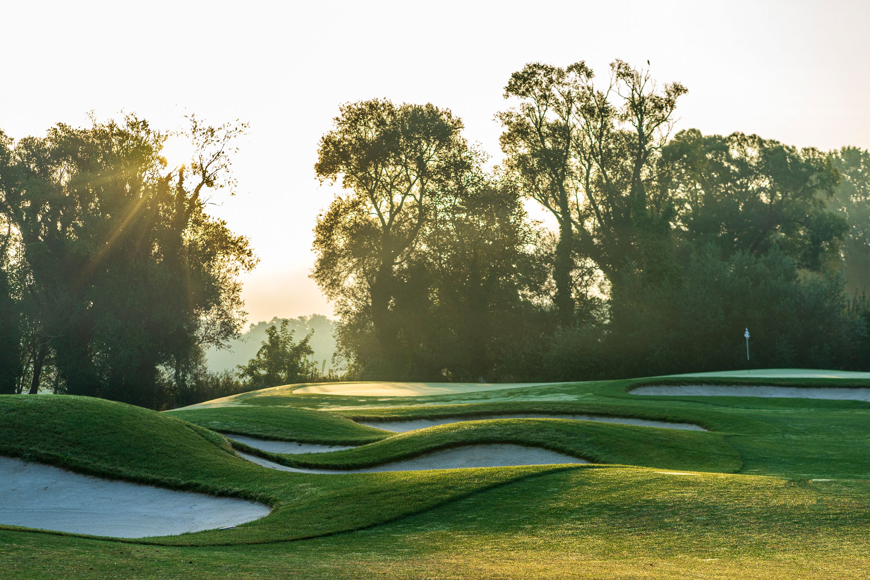 Un campo de golf con búnkeres de arena y árboles al fondo.