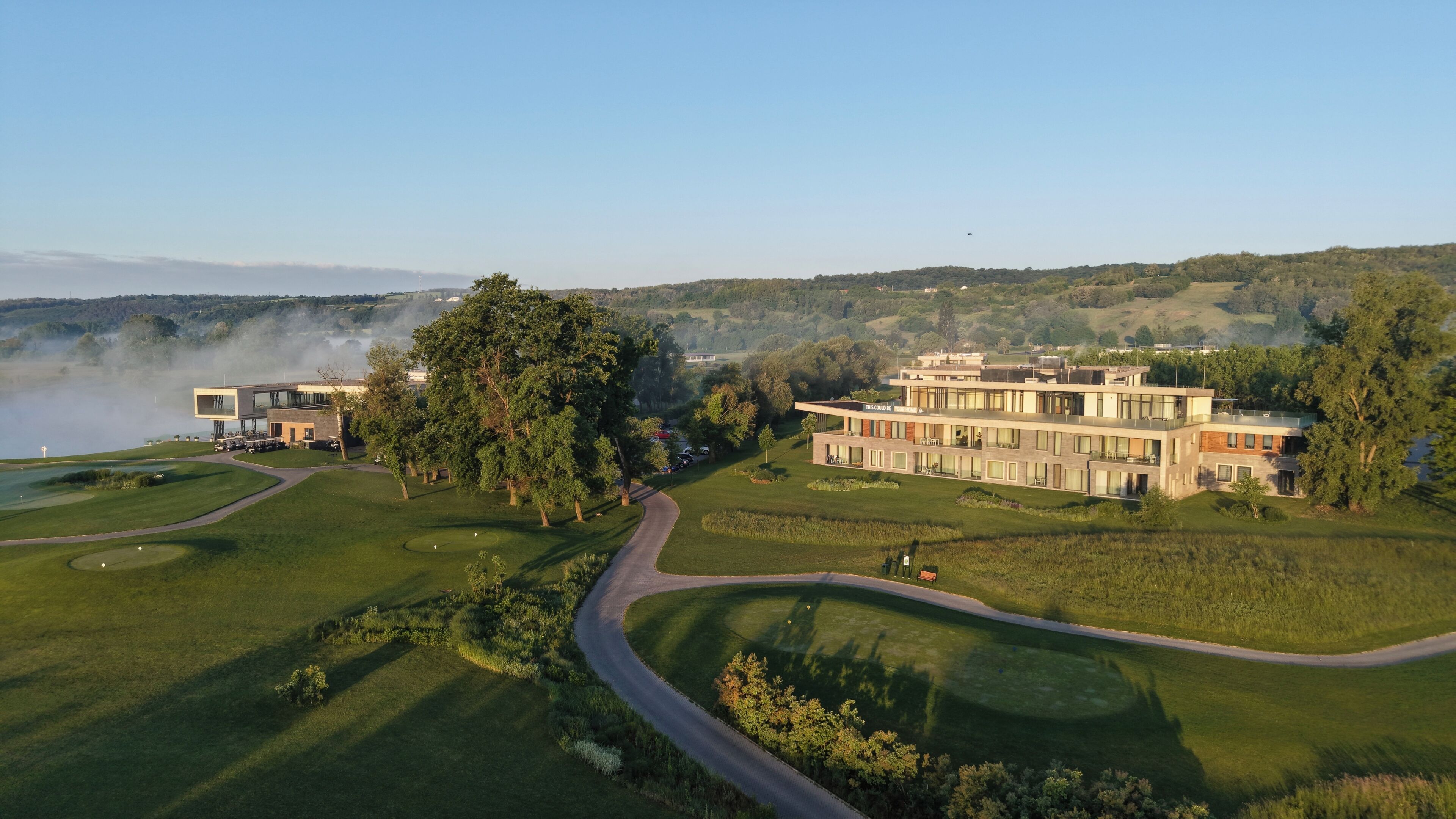 A modern building with multiple floors, surrounded by lush greenery and a golf course.