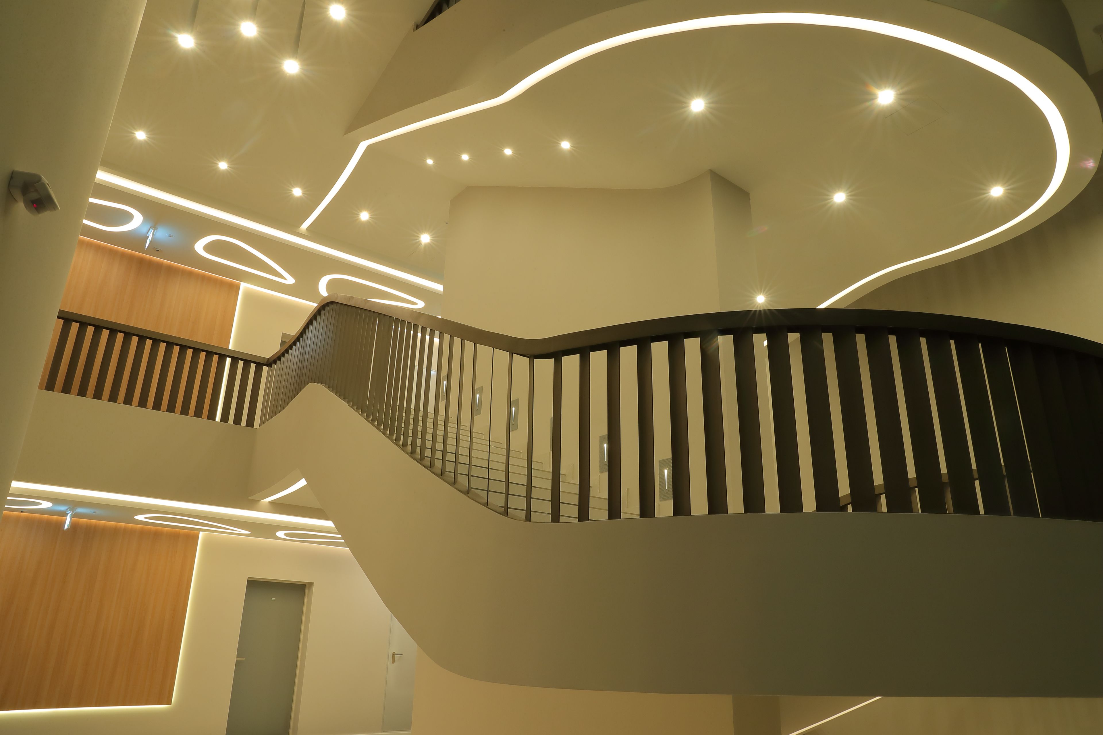 A modern interior with a curved staircase, recessed lighting, and a wooden panel wall.