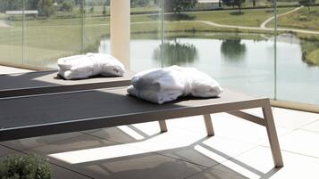 A balcony with a view of a lake and hills, two white towels on a bench, and a potted plant.