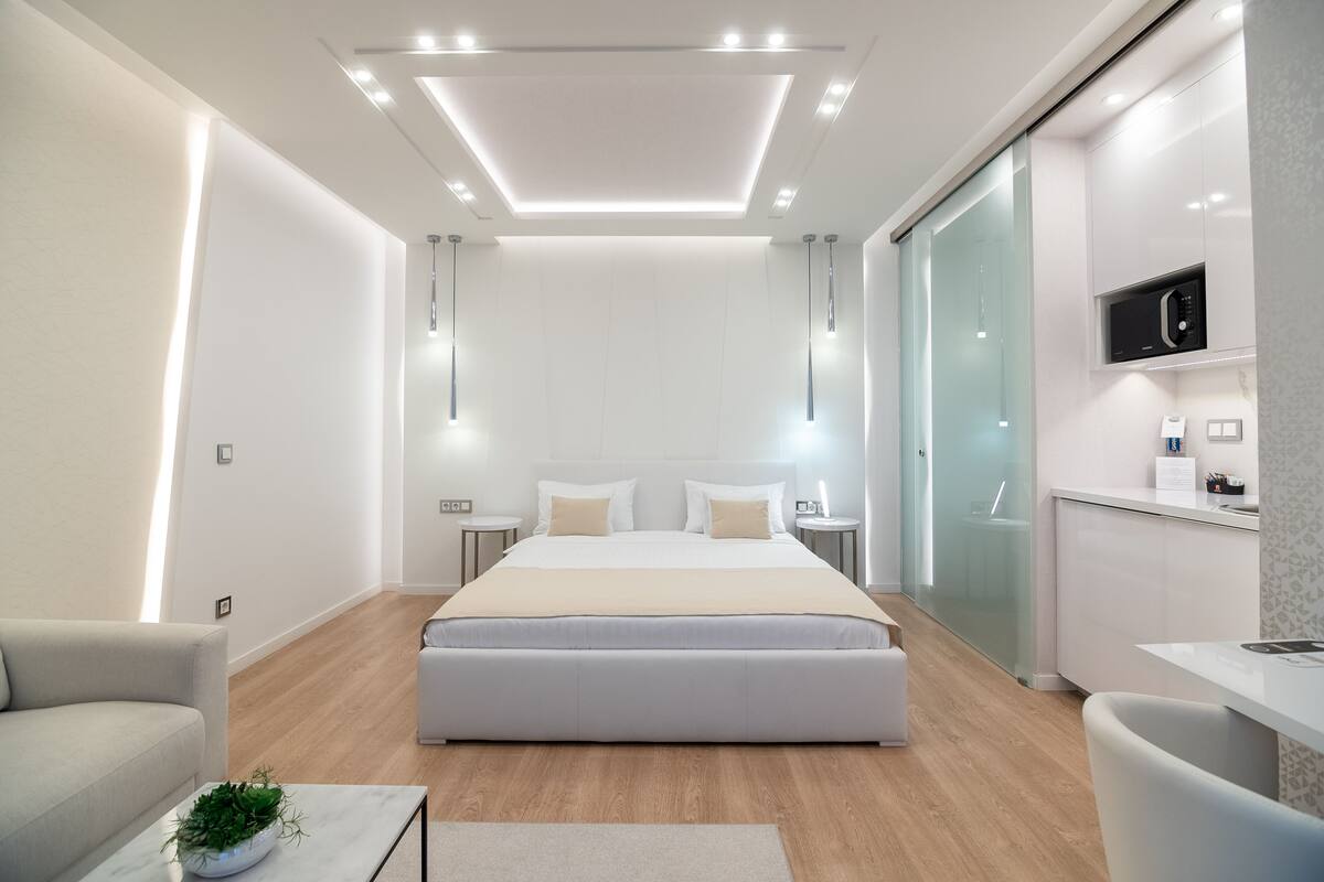 Un dormitorio moderno con una cama grande, mesitas de noche, televisor integrado y una zona de cocina con microondas.