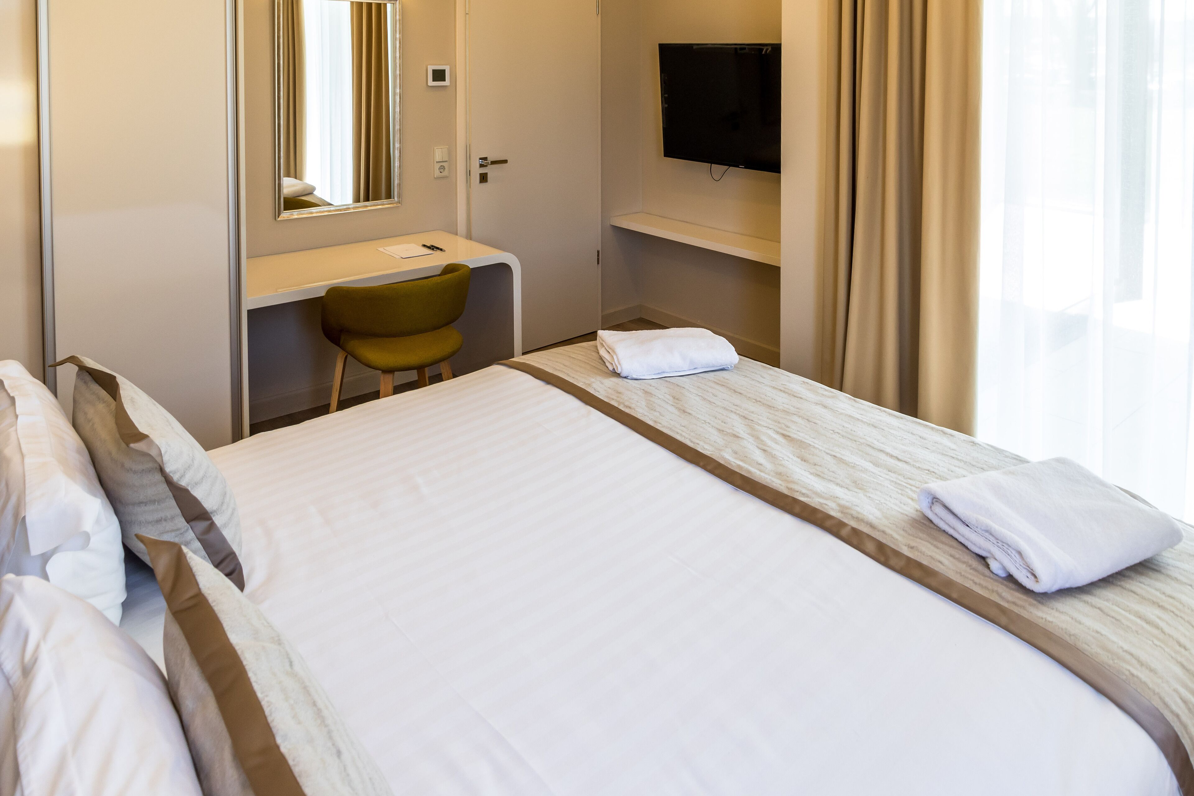 Habitación de hotel con cama, escritorio, silla, televisión y ventana con cortinas.