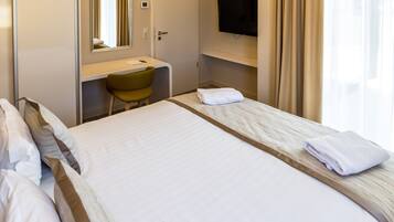 Habitación de hotel con cama, escritorio, silla, televisión y ventana con cortinas.