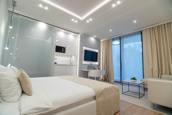 A modern hotel room with a large bed, a desk, a TV, and a balcony with curtains.