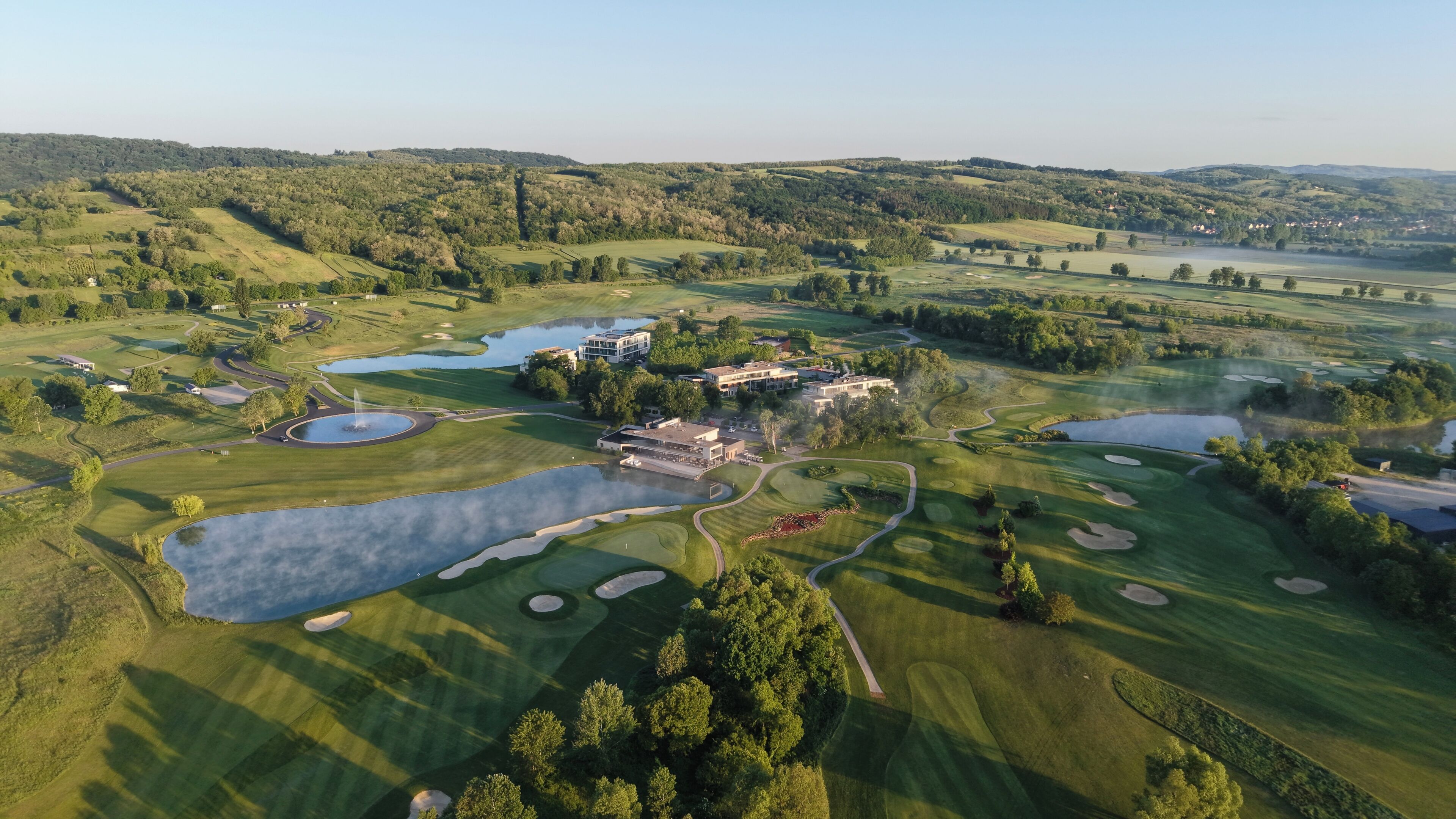 An aerial view of a golf course with multiple ponds, buildings, and surrounding hills.