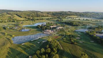 An aerial view of a golf course with multiple ponds, buildings, and surrounding hills.