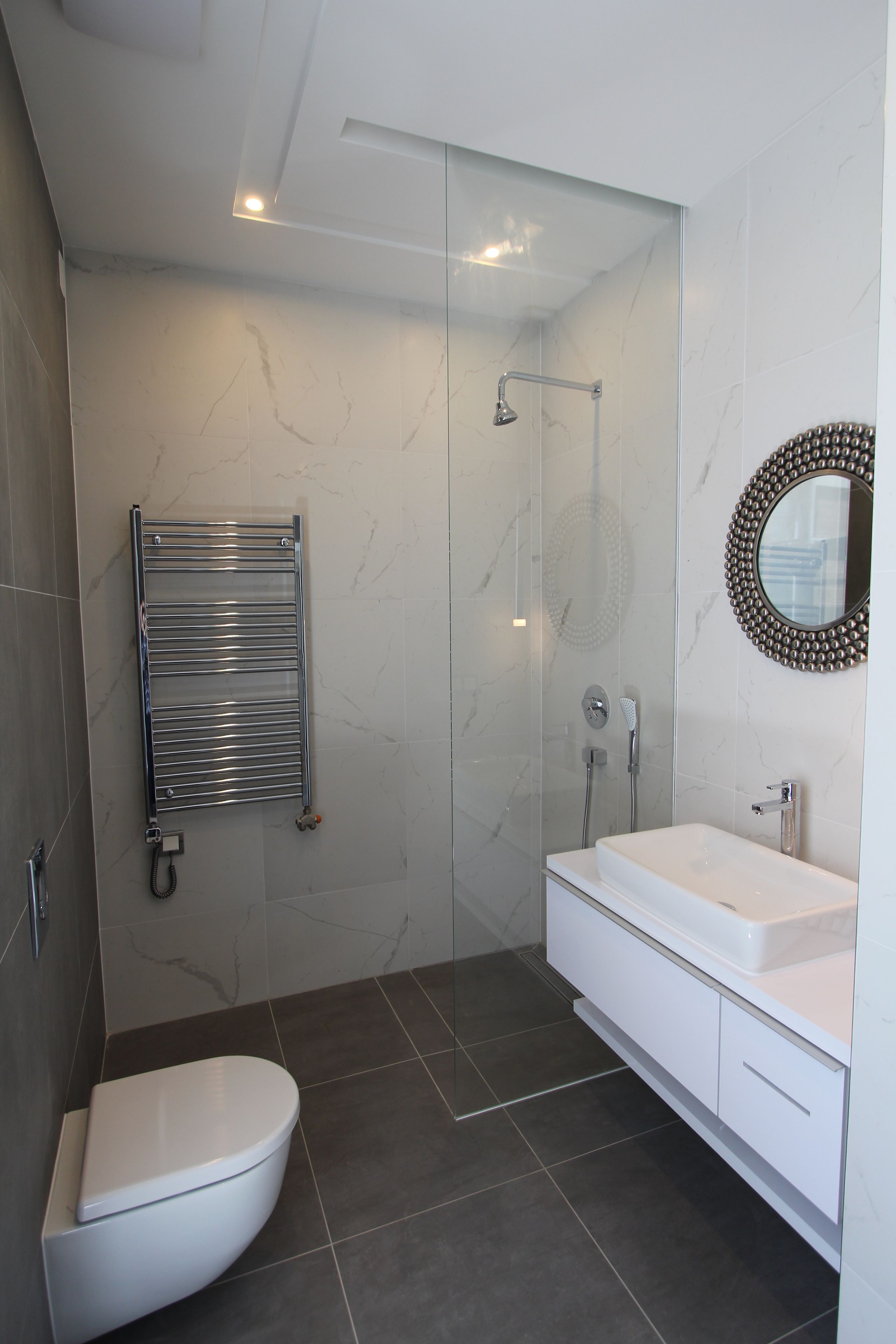 A modern bathroom with a glass-enclosed shower, a white toilet, and a vanity with a mirror.