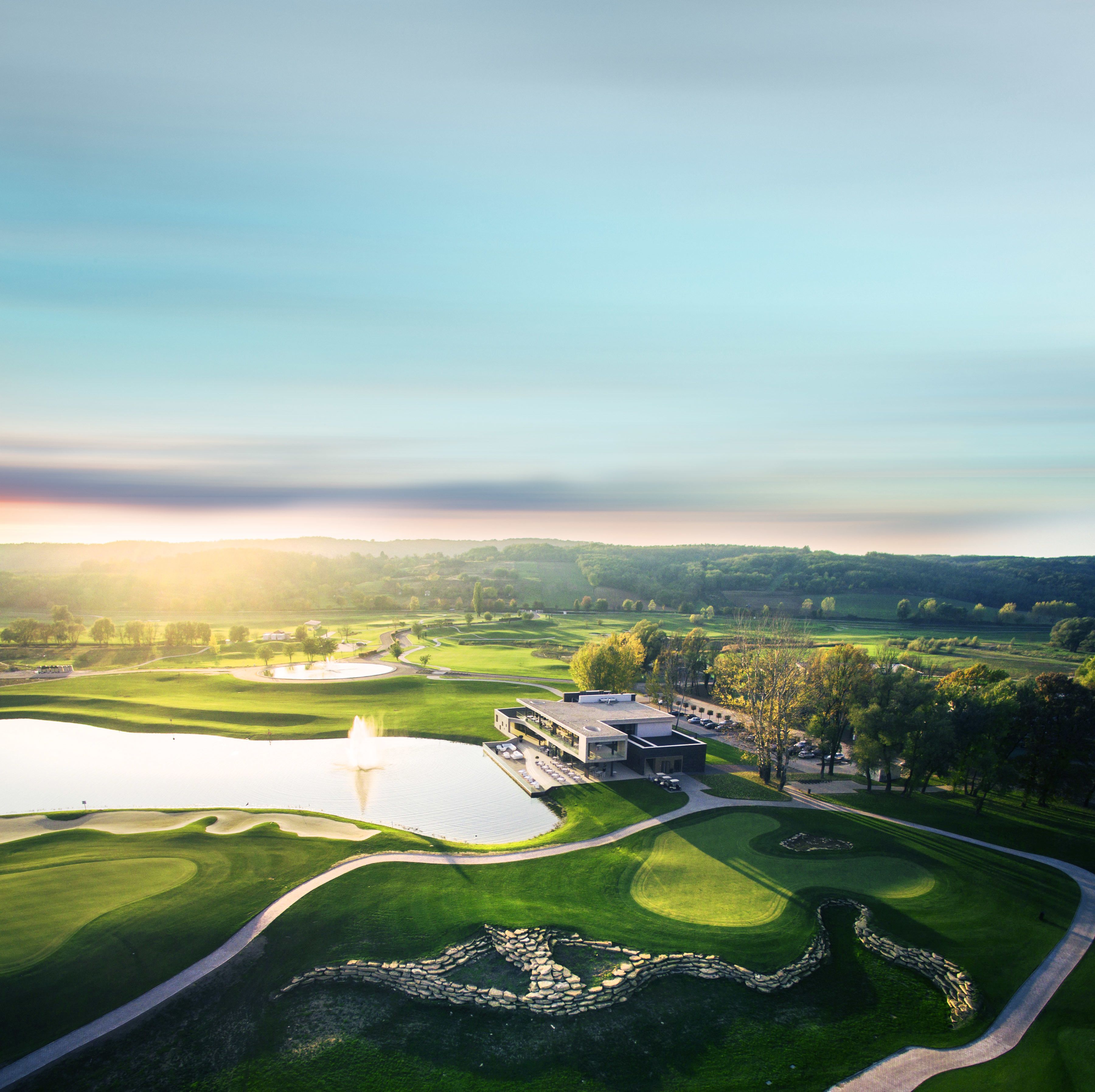 A golf course with a clubhouse, a pond, and a stone wall.