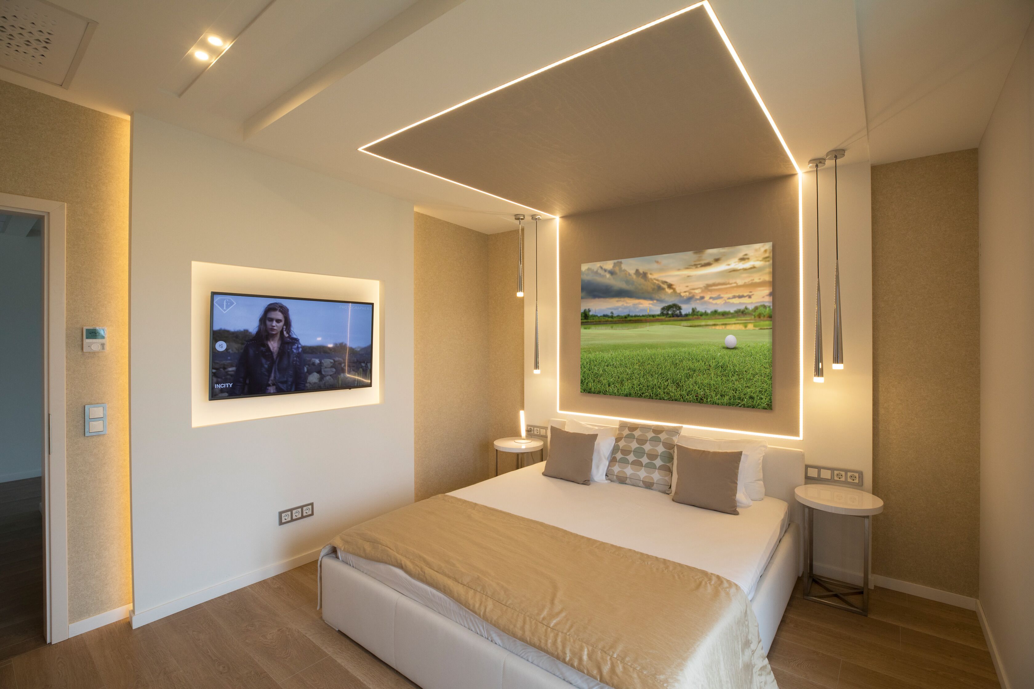 A modern bedroom with a large bed, a flat-screen TV mounted on the wall, and a painting of a golf course.