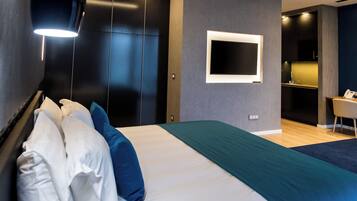 A modern hotel room with a large bed, dark walls, a TV mounted on the wall, and a small desk area.