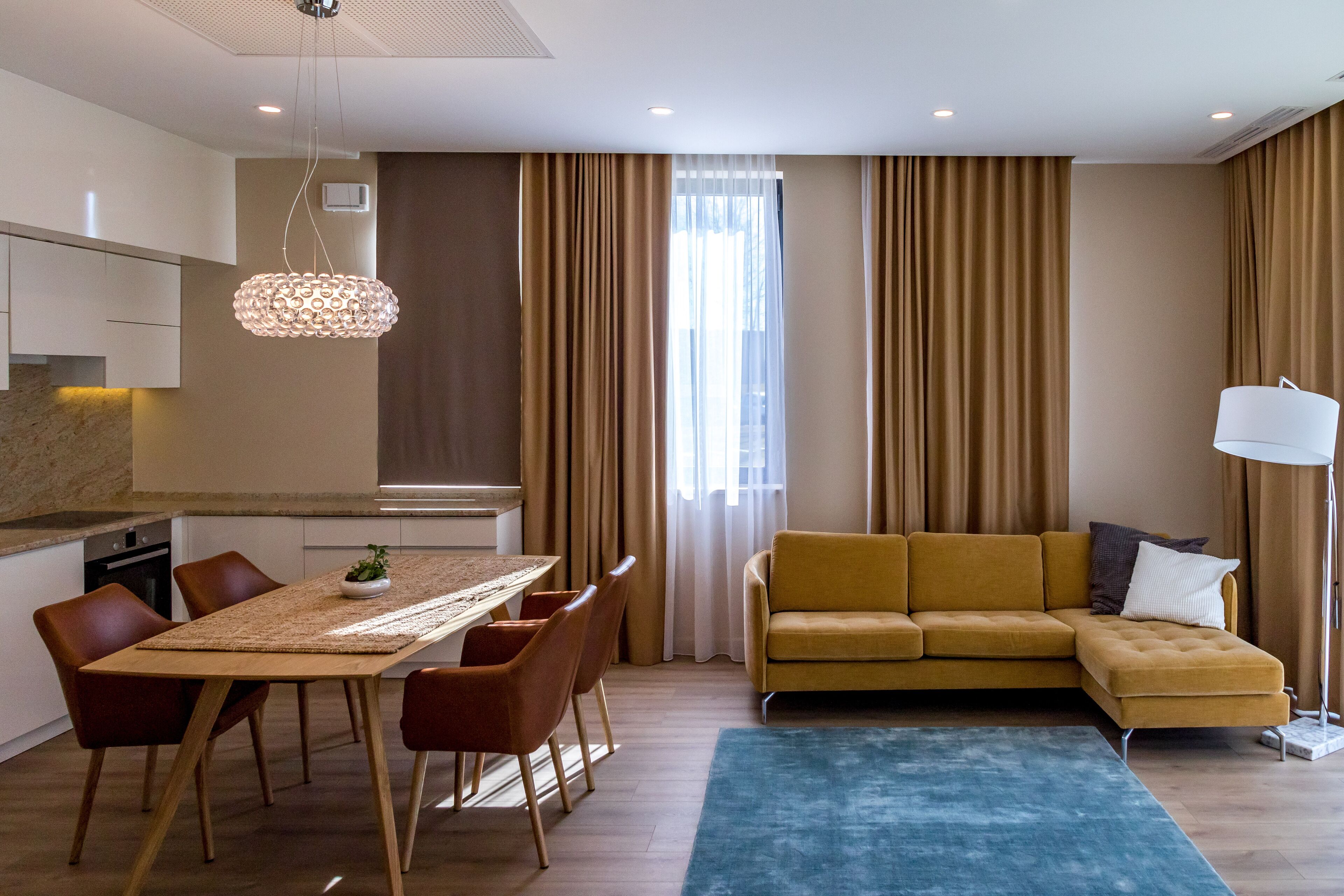 Een moderne woonkamer met een bank, eettafel, stoelen en een groot raam met gordijnen.
