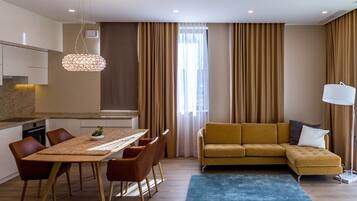 Een moderne woonkamer met een bank, eettafel, stoelen en een groot raam met gordijnen.