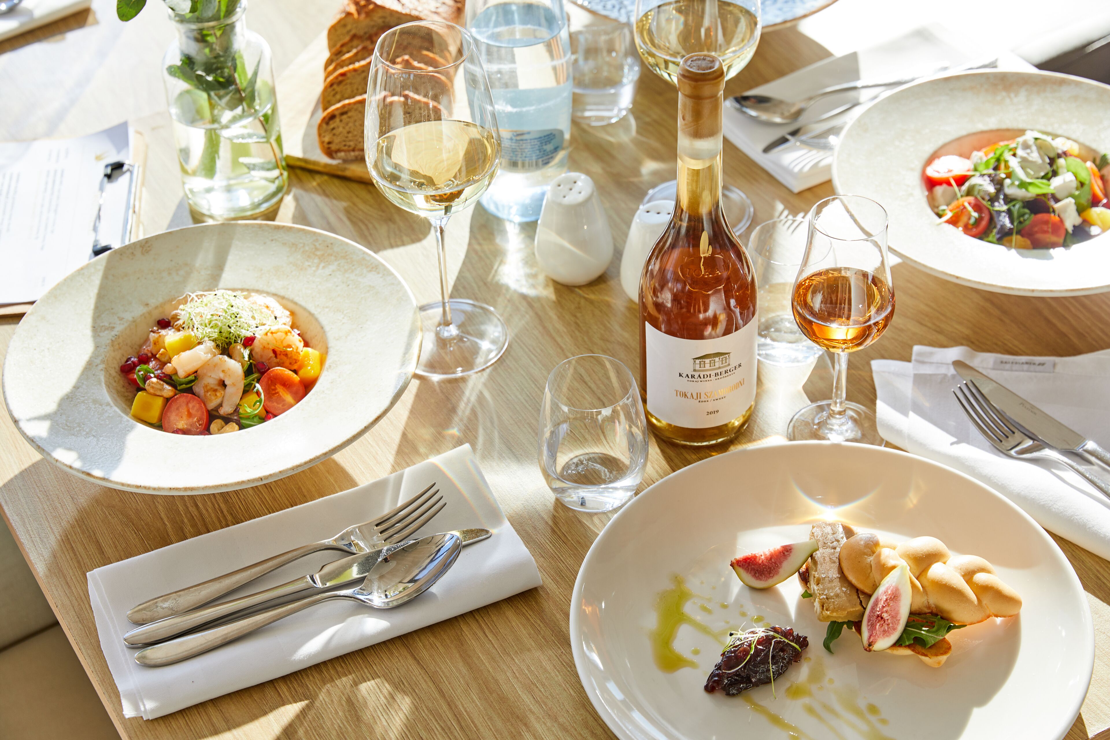 Una mesa de comedor con varios platos de comida, copas de vino y cubiertos.