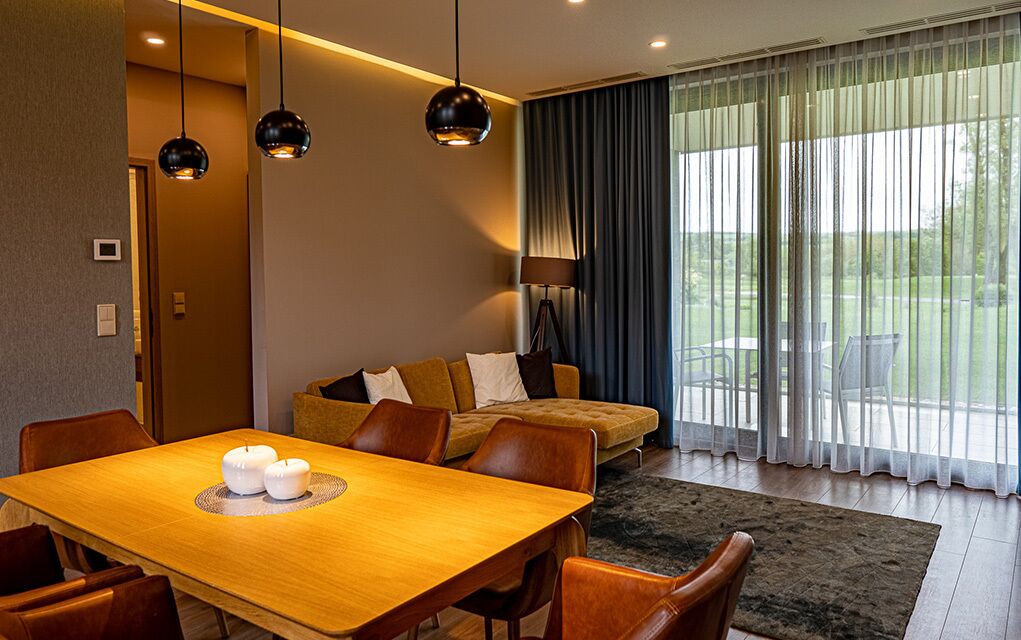 Ein modernes Hotelzimmer mit Essbereich, einer Couch und einem großen Fenster mit Vorhängen.