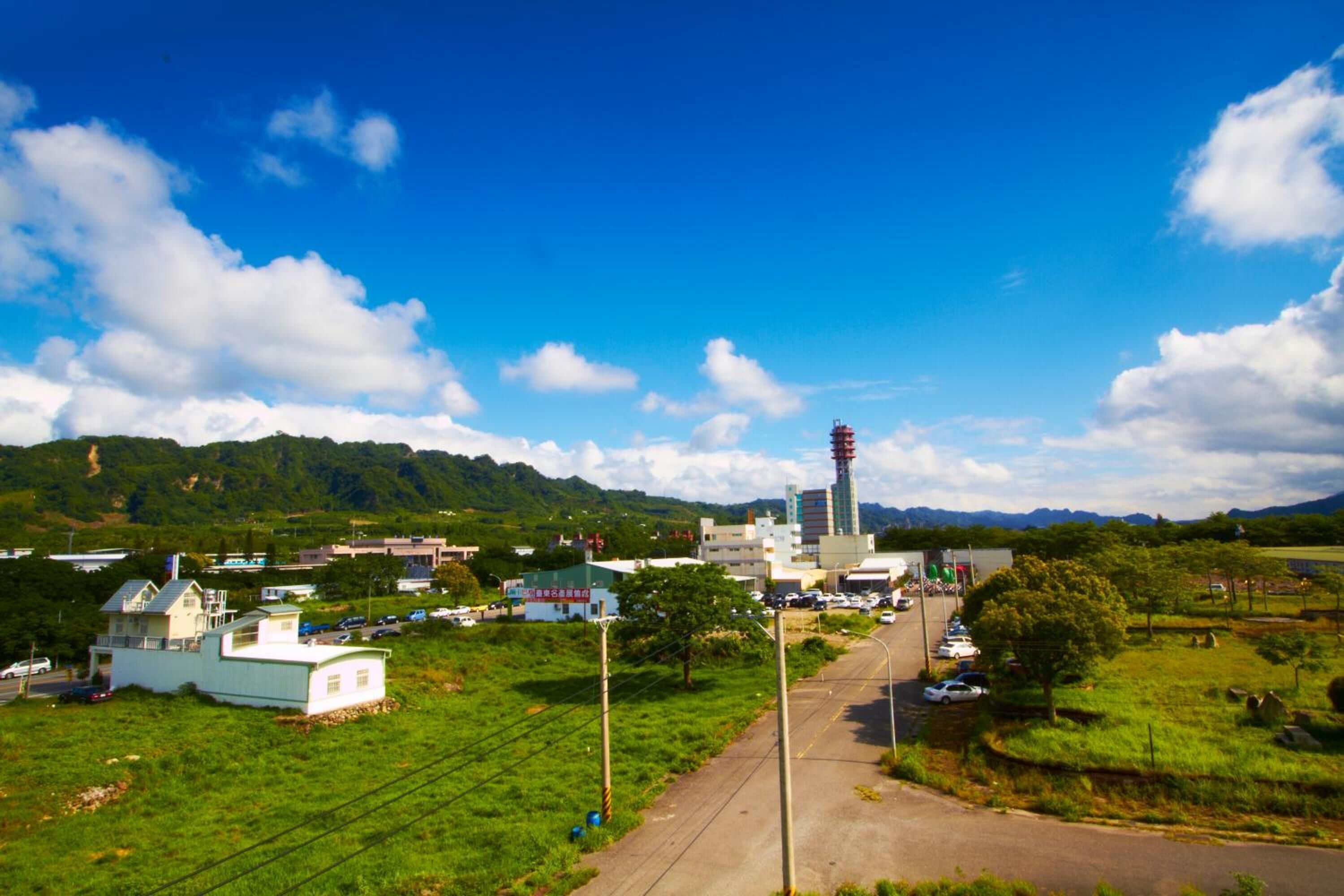 A rural landscape with a road, buildings, and a tower.
