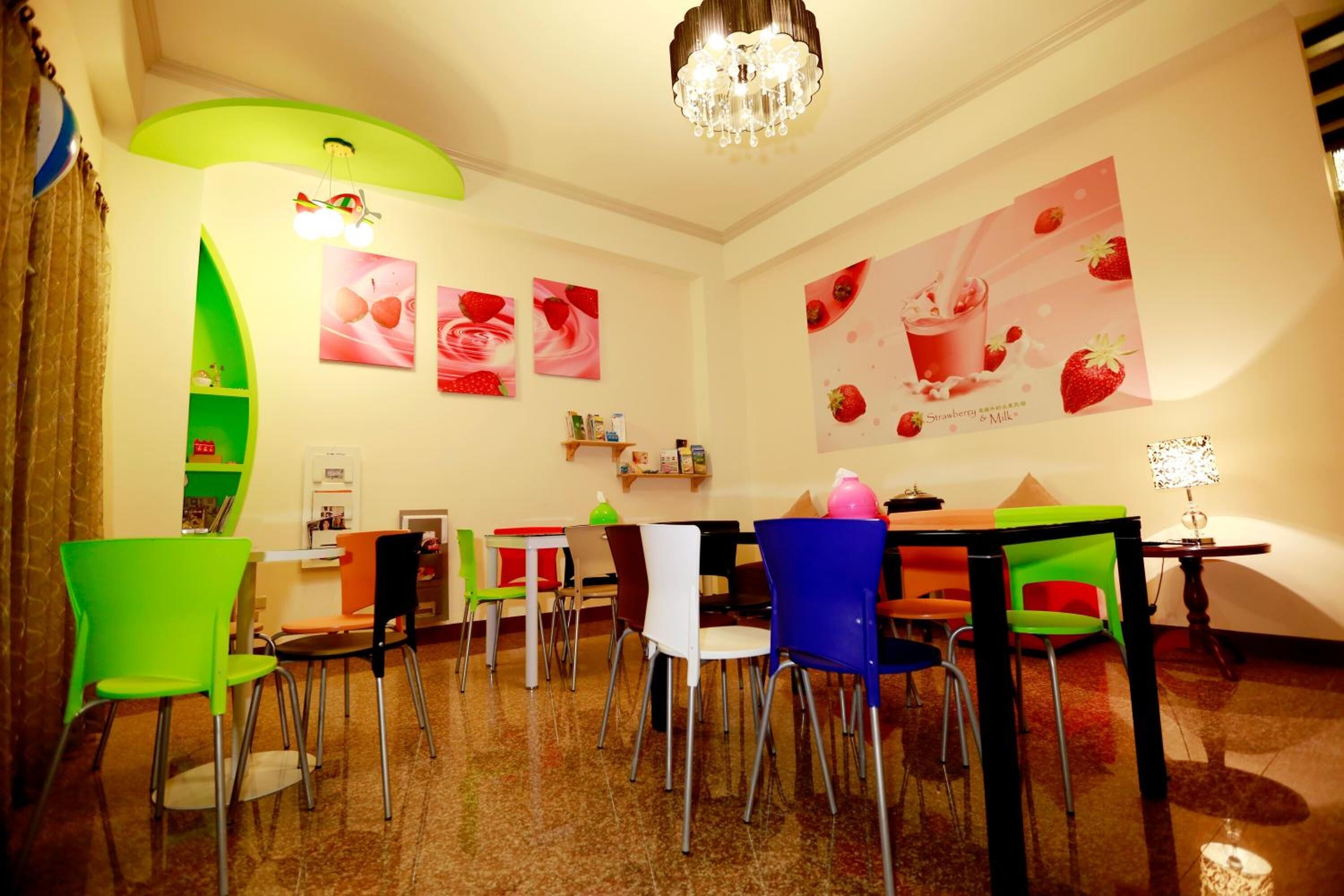 A dining area with colorful chairs and tables, a chandelier, and wall art featuring strawberries.