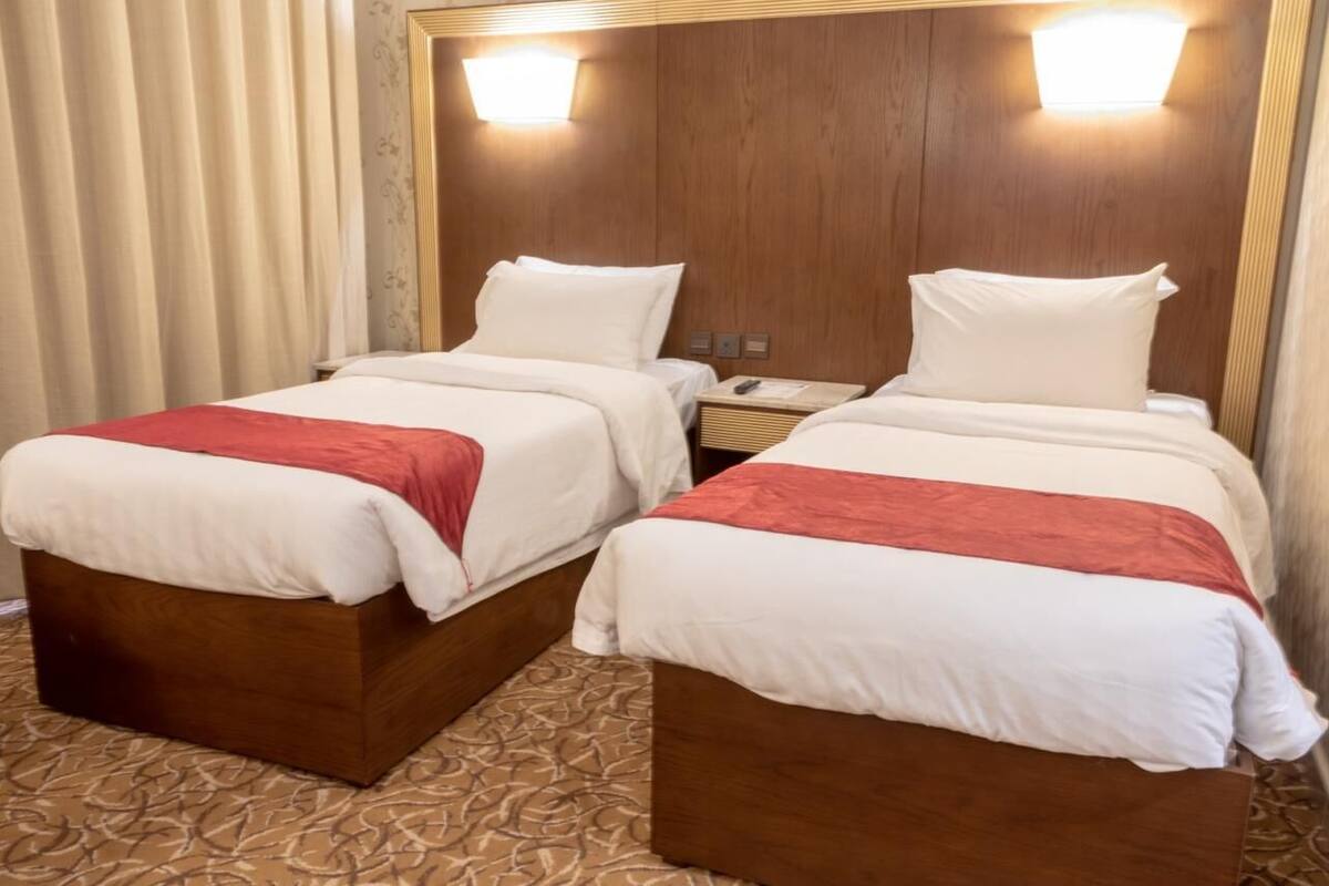 A hotel room with two beds, each with a wooden headboard, white bedding, and a red accent.