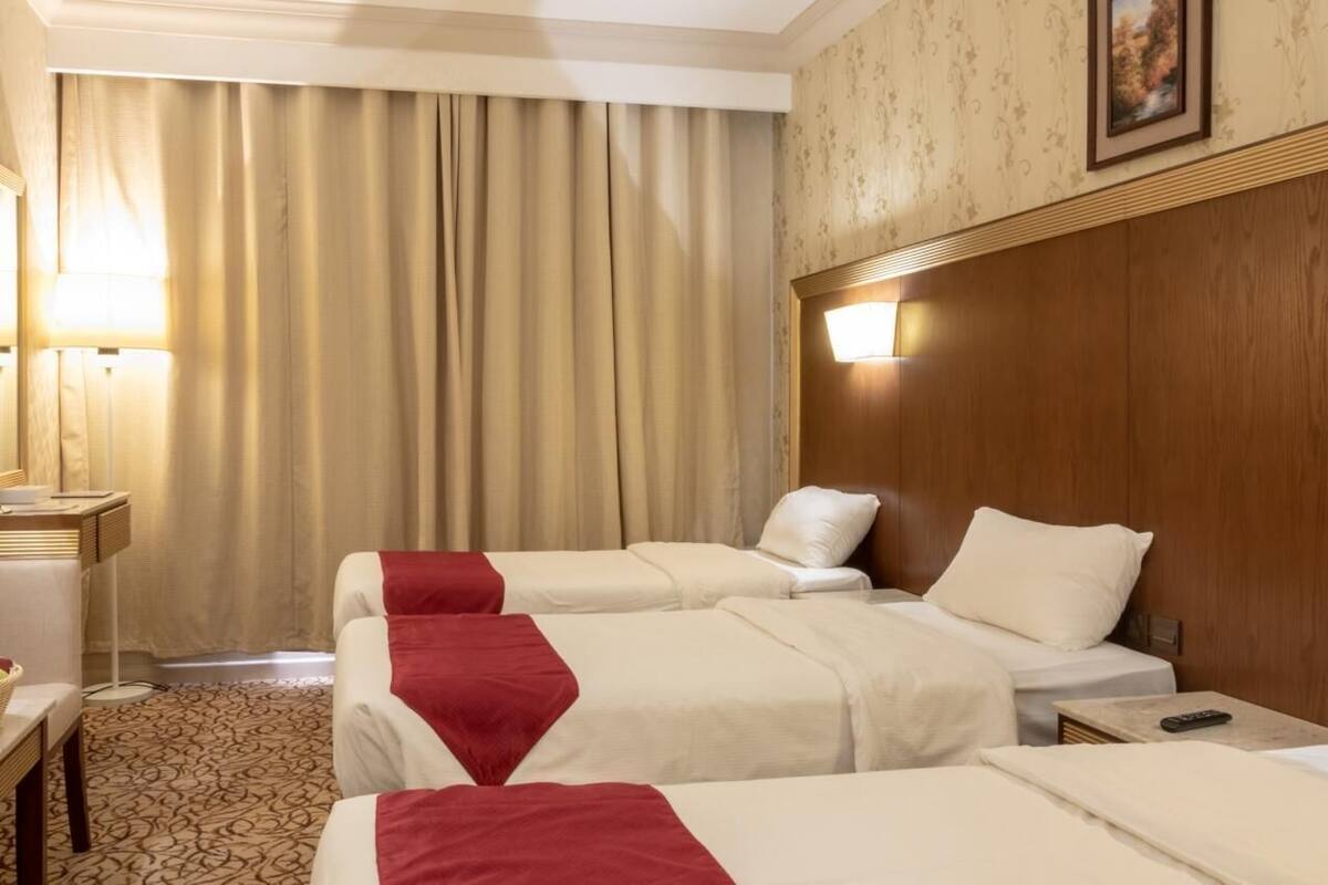 A hotel room with two beds, a desk, a lamp, and a painting on the wall.