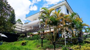 A white house with a covered patio area, surrounded by lush greenery and various plants. - Hotel Tierra Maravilla (Salento)