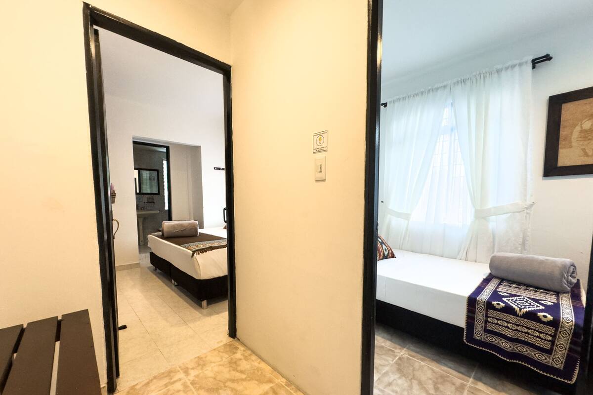 Quarto de hotel com uma cama, mesa de cabeceira, cadeira e janela com cortinas.
