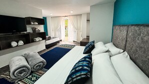 A modern hotel room with a large bed, a TV, a sofa, and a balcony with curtains. - Hotel Tierra Maravilla (Salento)