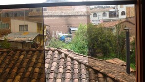 Vista desde una ventana sobre una zona residencial con tejados de tejas rojizas, un coche aparcado y un cartel que dice 'Noticias'.