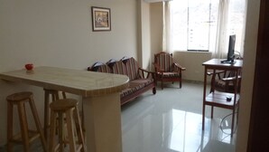 Una sala de estar con un sofá, una mesa de comedor con taburetes, un televisor y una ventana con cortinas.