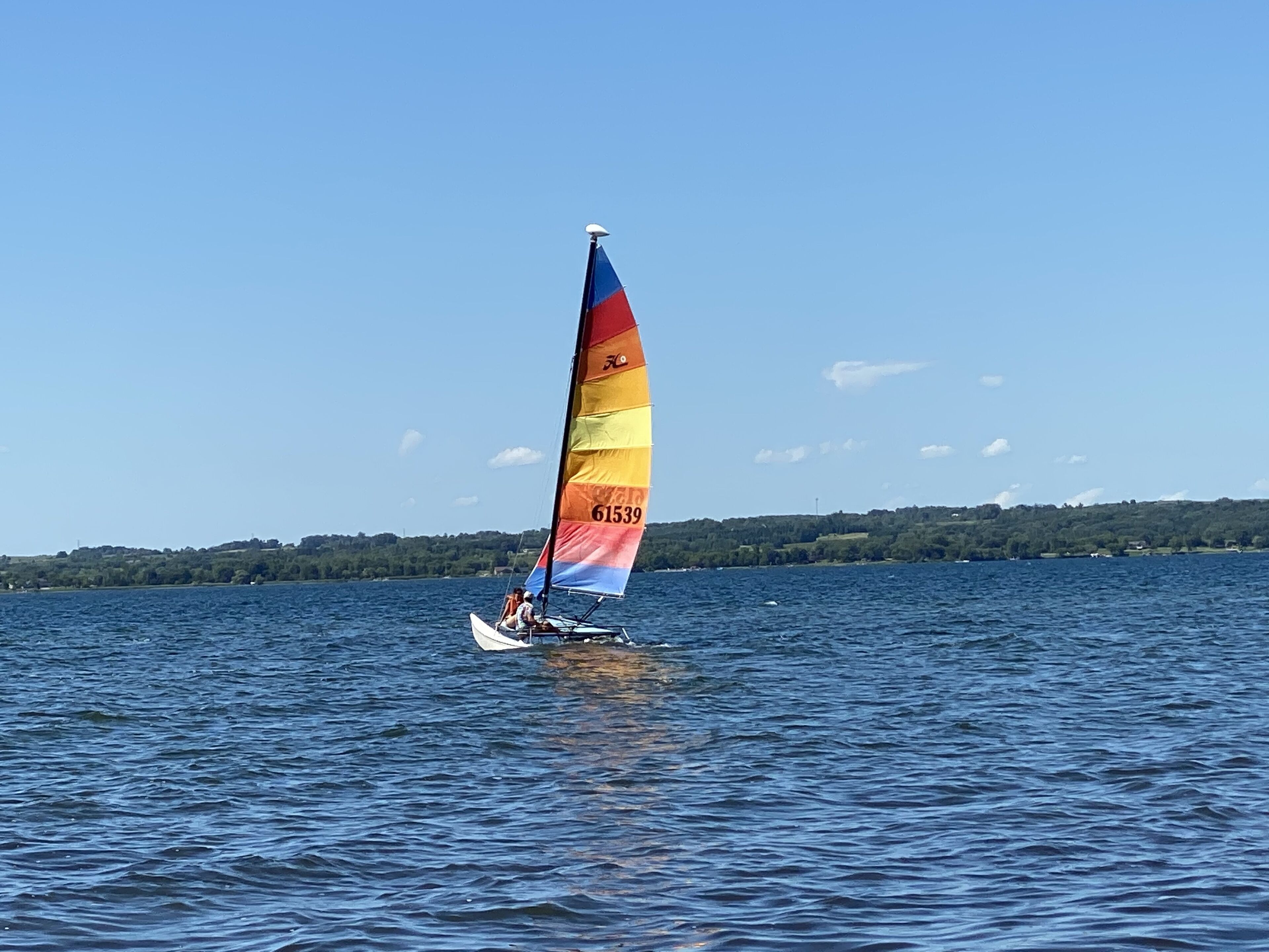 Ein Segelboot mit einer bunt bemalten Segel auf ruhigem Gewässer.