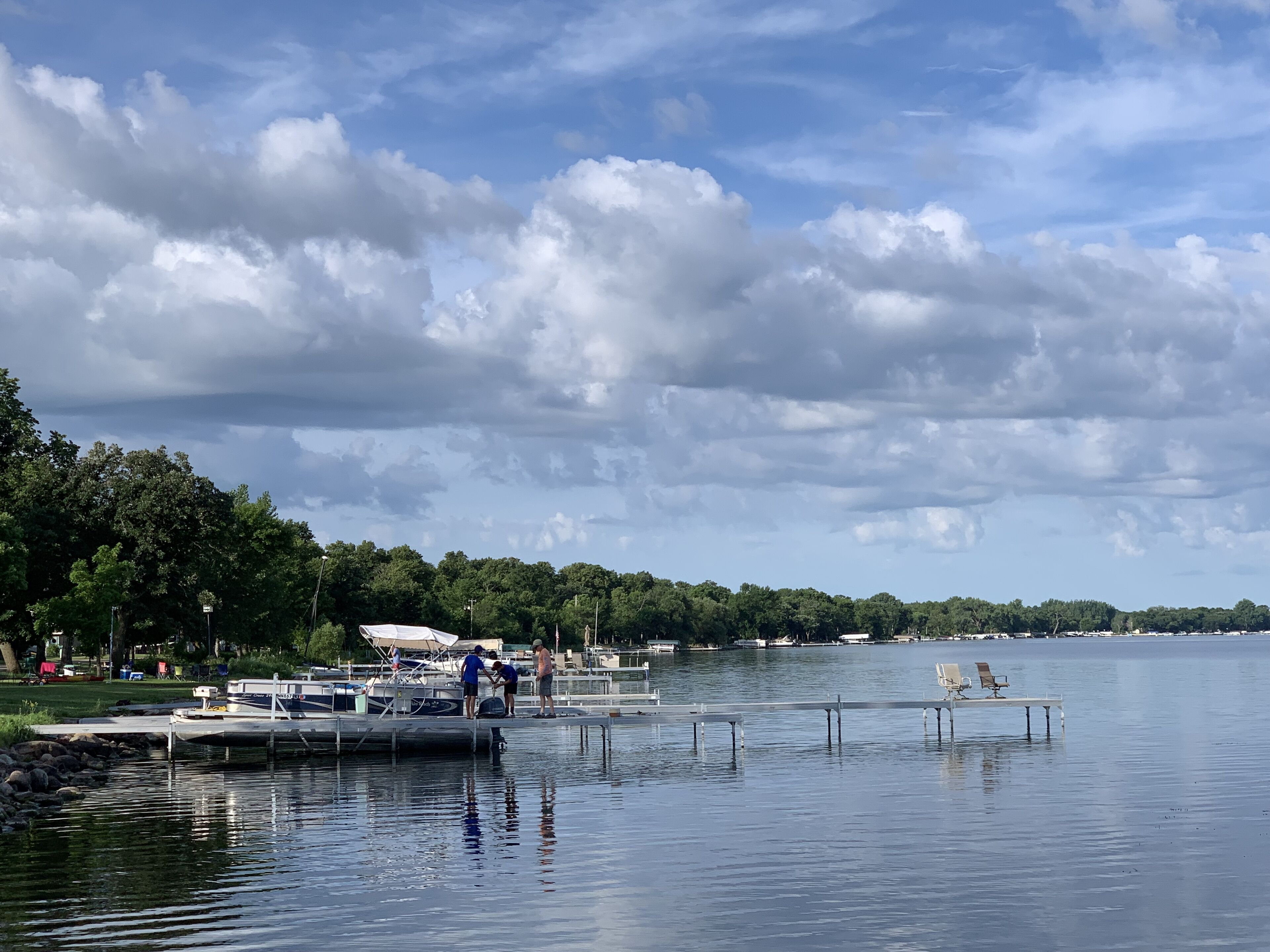 A marina with boats docked, a dock with people, and a calm lake.