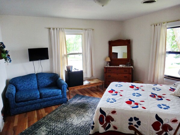 A bedroom with a bed, a blue sofa, a dresser, a TV, and a window with curtains. - Peters Sunset Beach Resort (Glenwood)