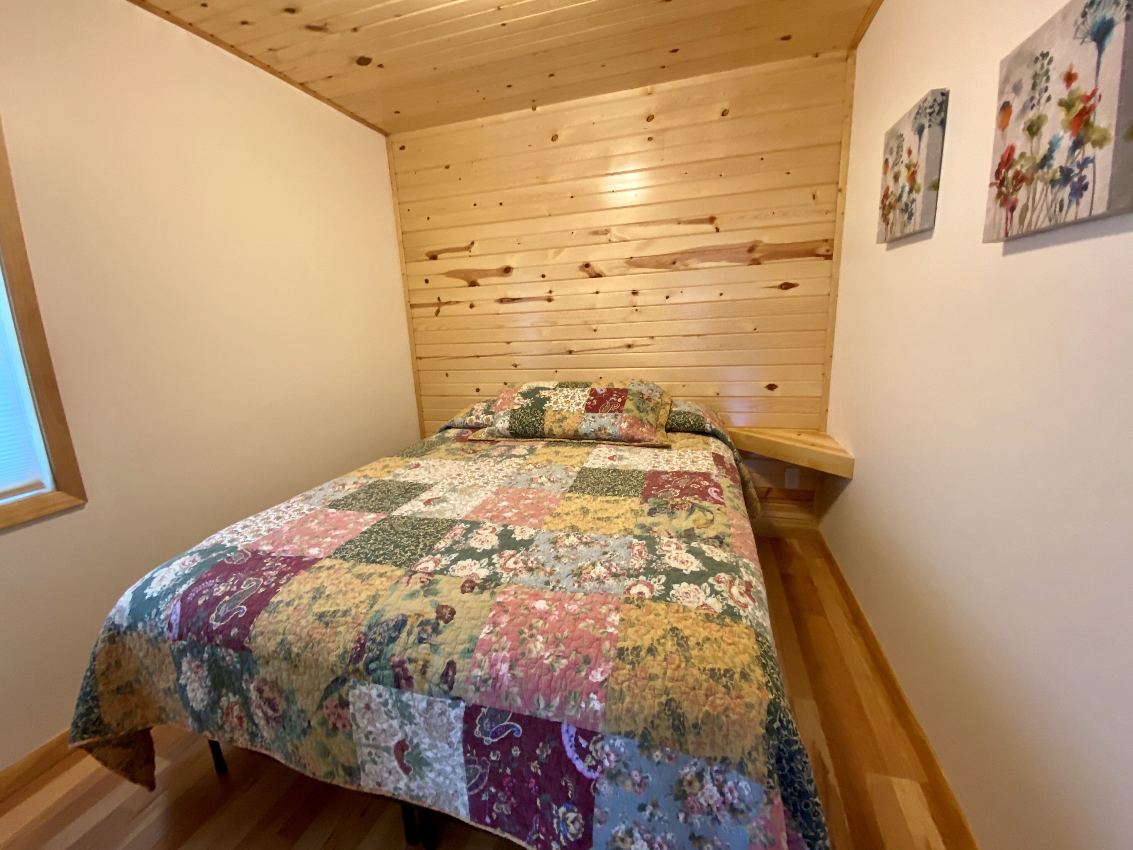 Un dormitori amb sostre de fusta, un edredó floral i dos quadres penjats a la paret.