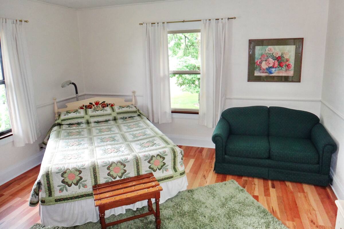 Ein Schlafzimmer mit einem Bett, einem grünen Sofa, einer Holzbank und einem Gemälde an der Wand.