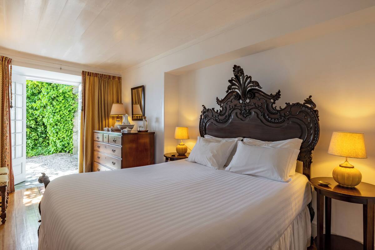 A neatly made bed with white linens, a wooden headboard, and two bedside lamps.