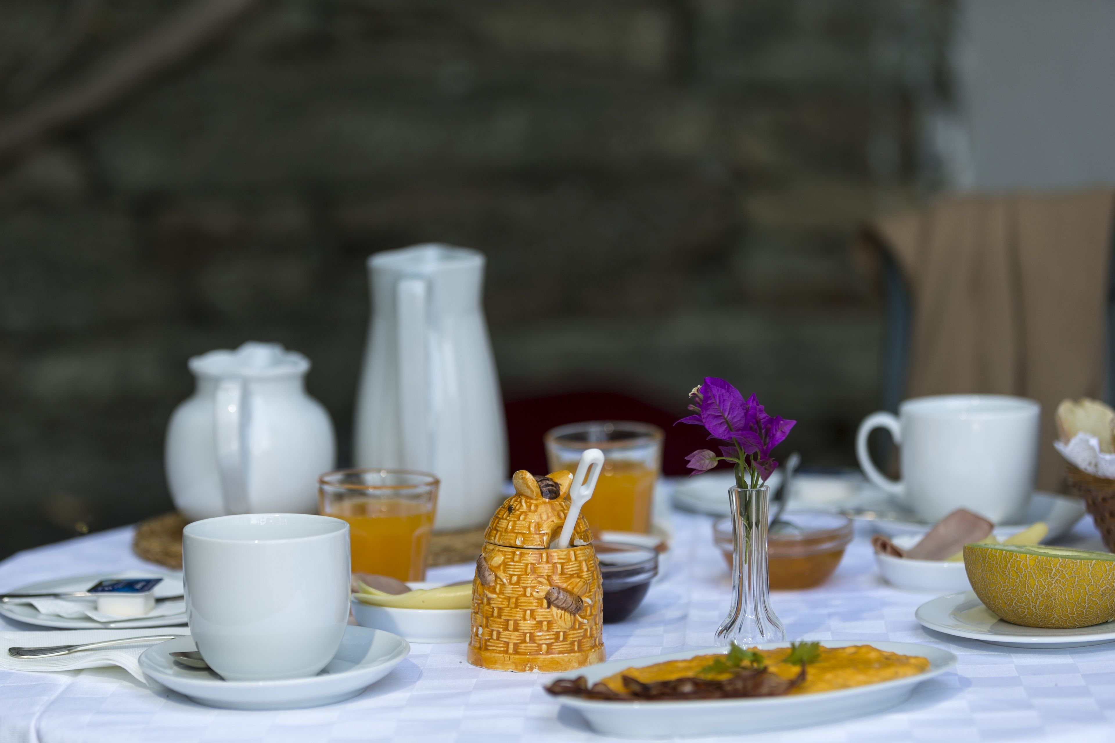 A breakfast table with various dishes, cups, and a vase with a flower.
