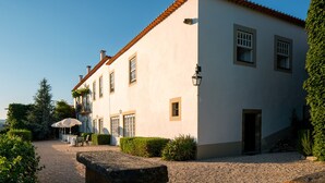 A two-story building with a tiled roof, a stone pathway, and a garden area with tables and chairs.