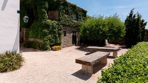 A stone building partially covered with ivy, a gravel courtyard, and a stone bench.