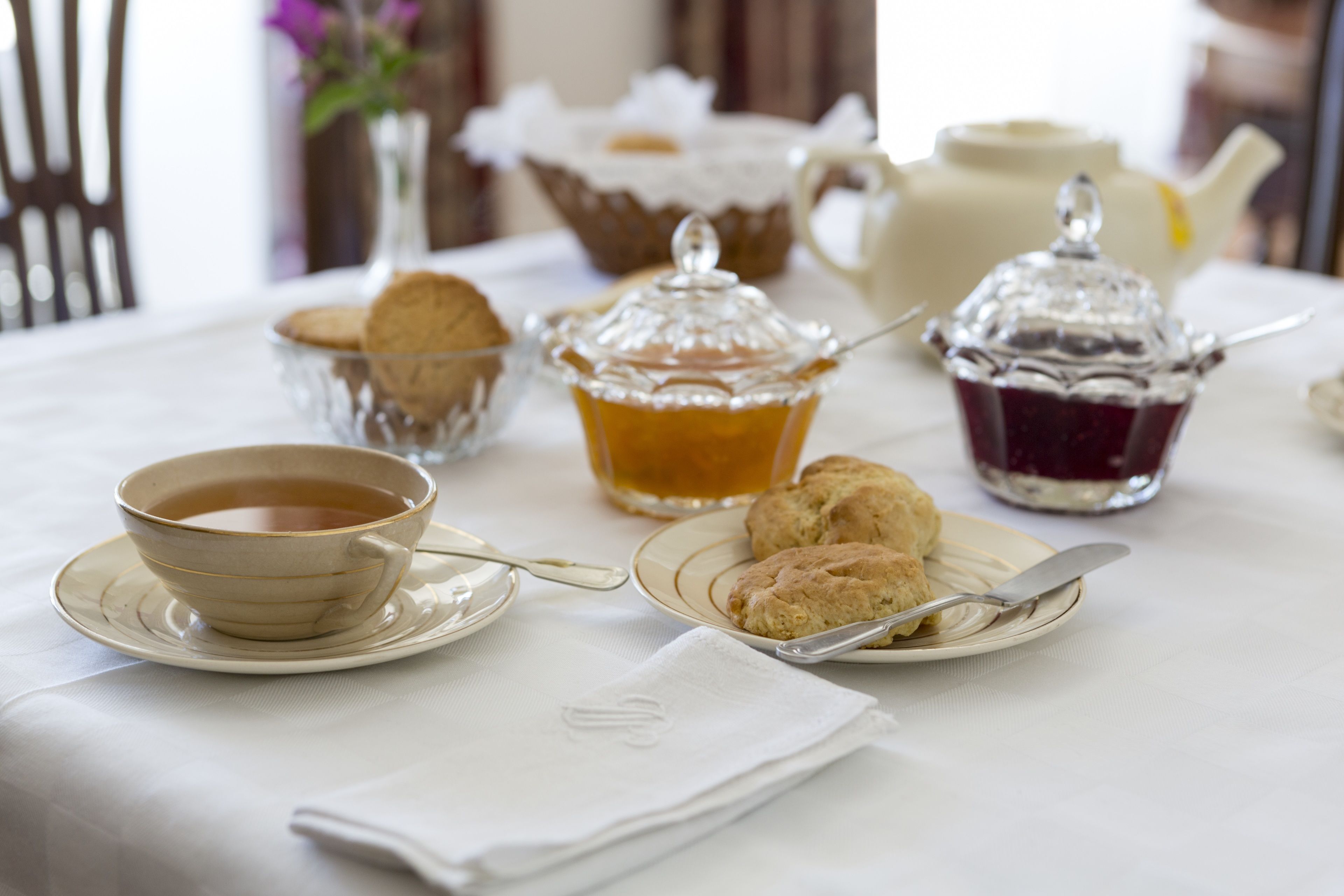 Una mesa dispuesta con una taza de té, galletas y dos recipientes de mermelada.