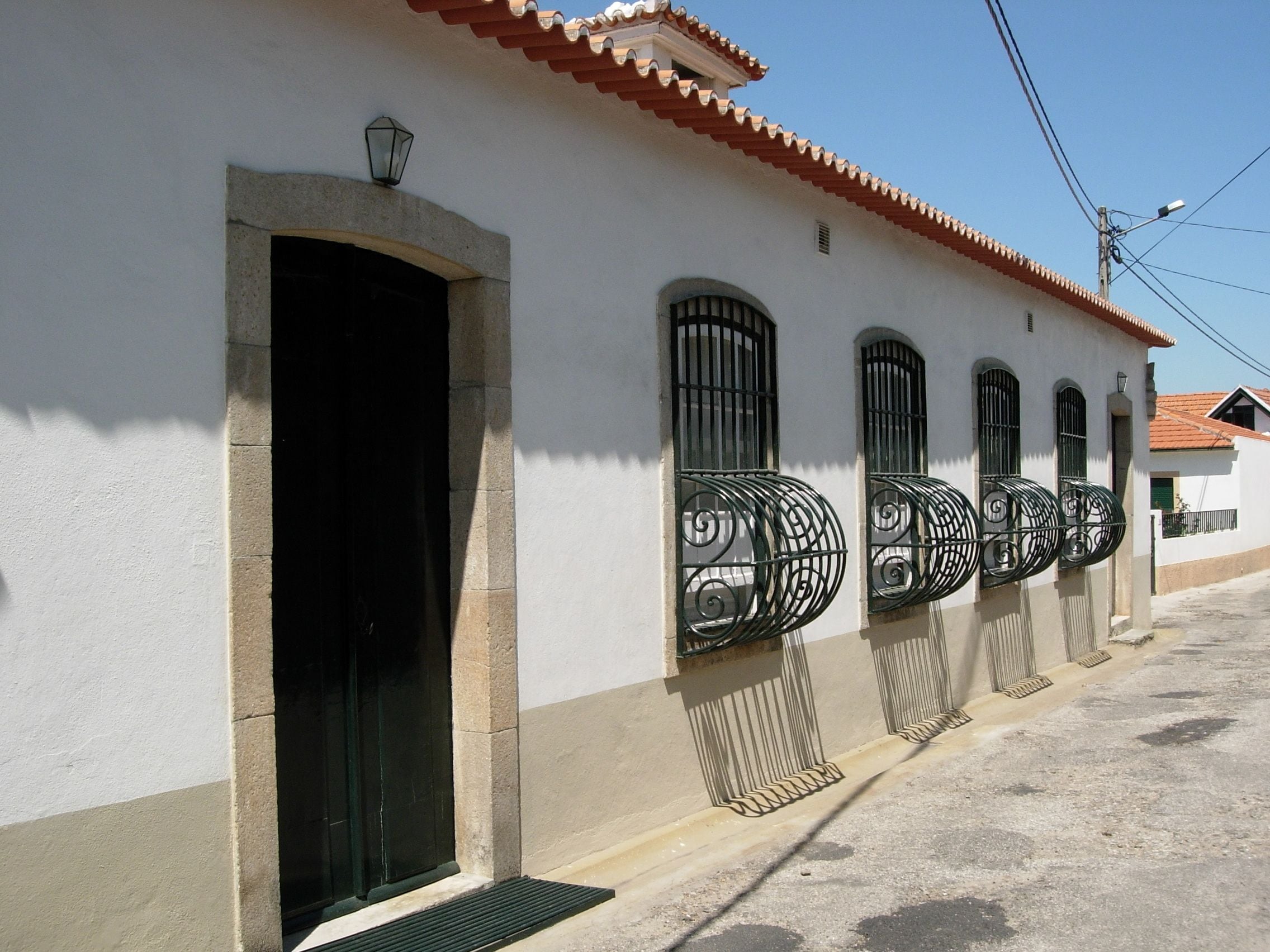 A building with a white facade, a red-tiled roof, and a series of windows with decorative iron grilles.