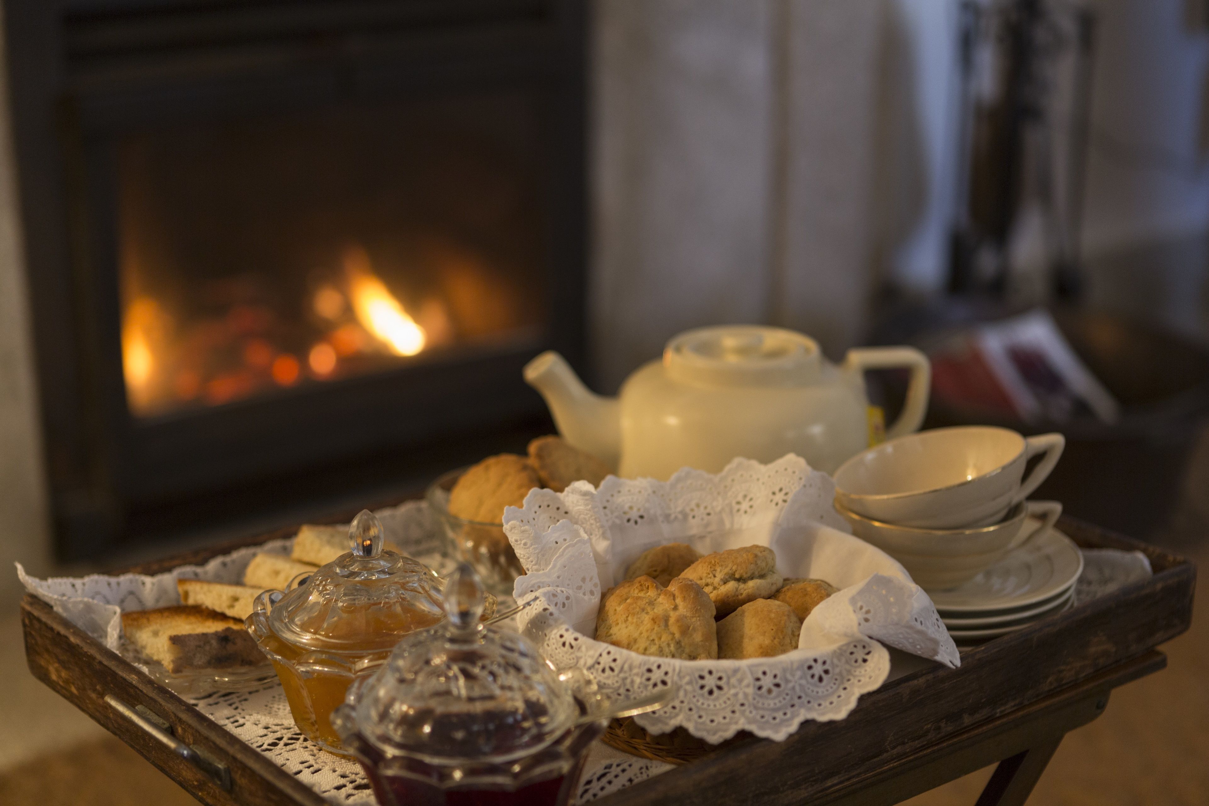 Un plateau avec du pain, des biscuits, une théière et un pot de confiture, posé devant une cheminée.