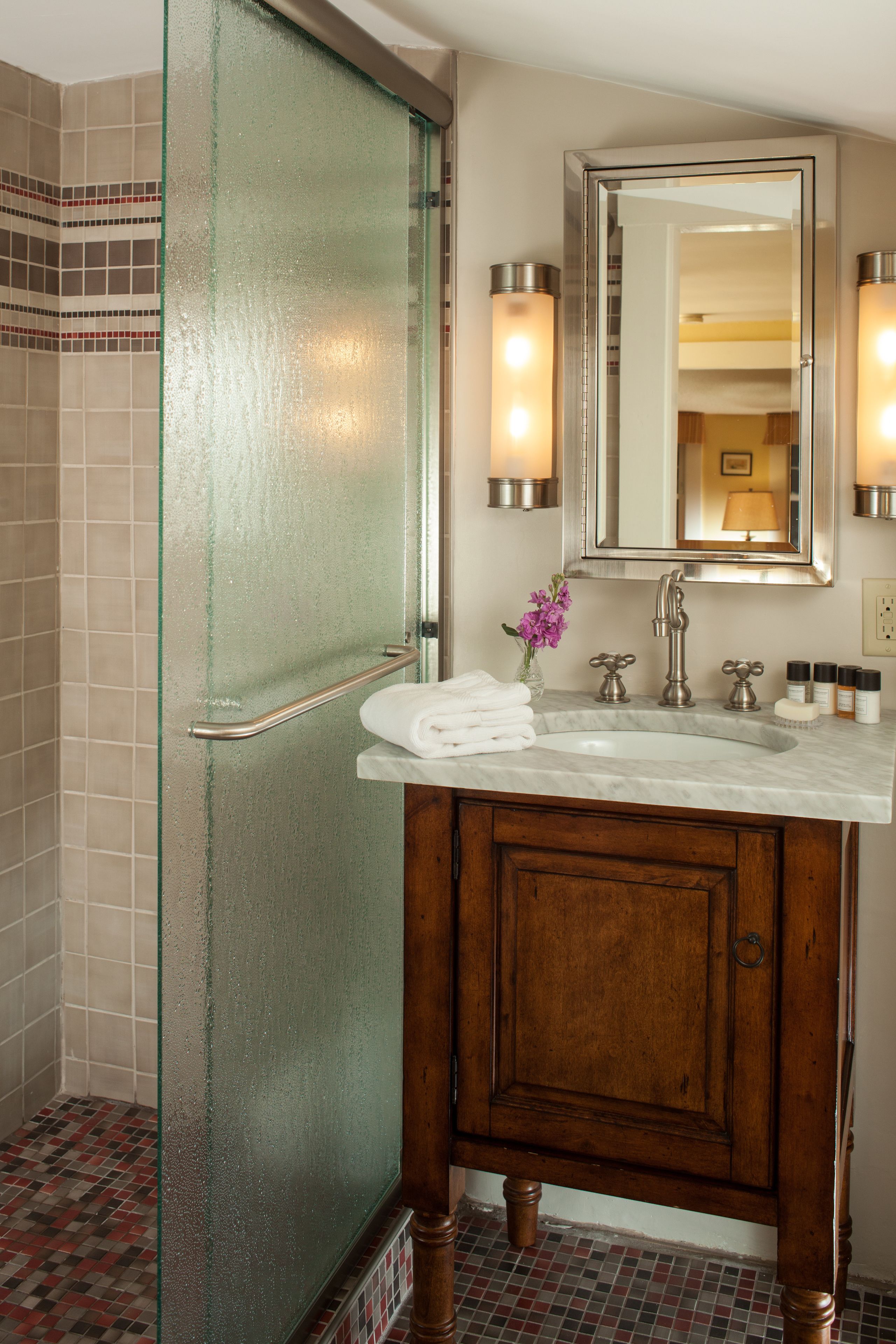 A bathroom with a glass shower door, a wooden vanity, a sink, and a mirror.